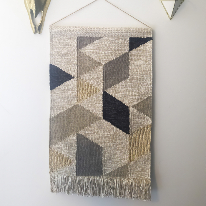 Square frame Woven tapestry metal bull head and plant hanger decorations against white wall. The woven wall hanger has a geometric pattern design and fringes.